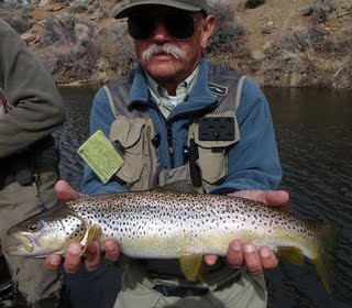 Large Brown held up by an Man in a Mustache on the bank of the RIver