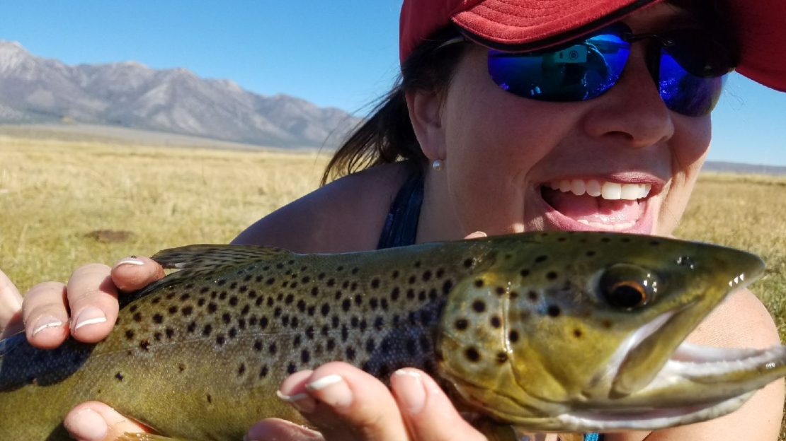 Happy female angler holds a large brown trout