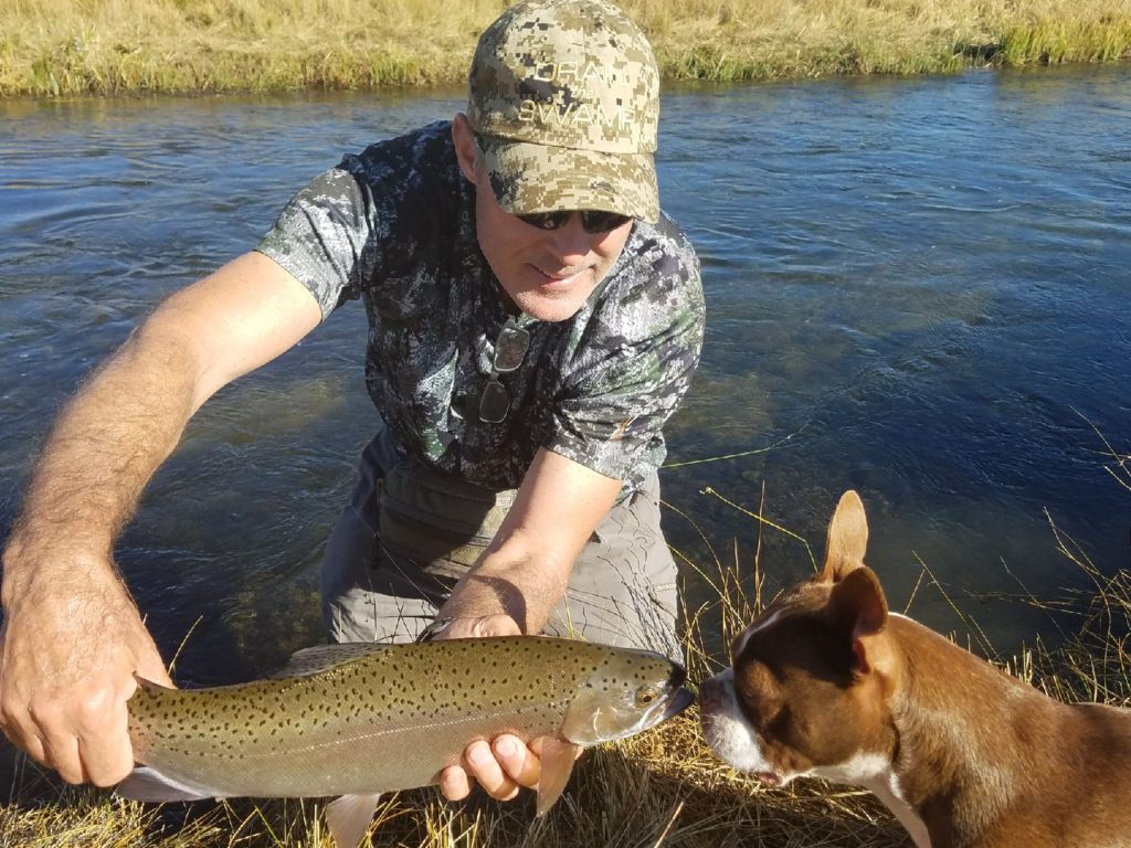 Large brown trout on upper river kisses small Boston terrier 