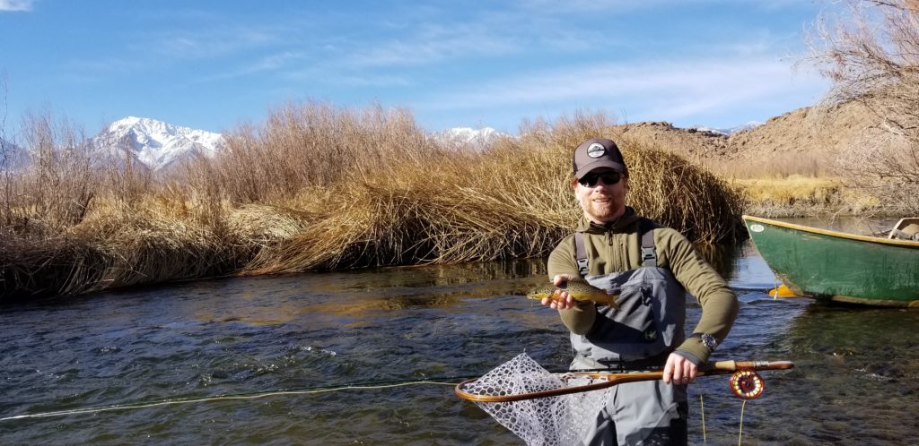 Angler holds up a nice brown trout on the lower Owens River with Mount Tom in the background and a green drift boat