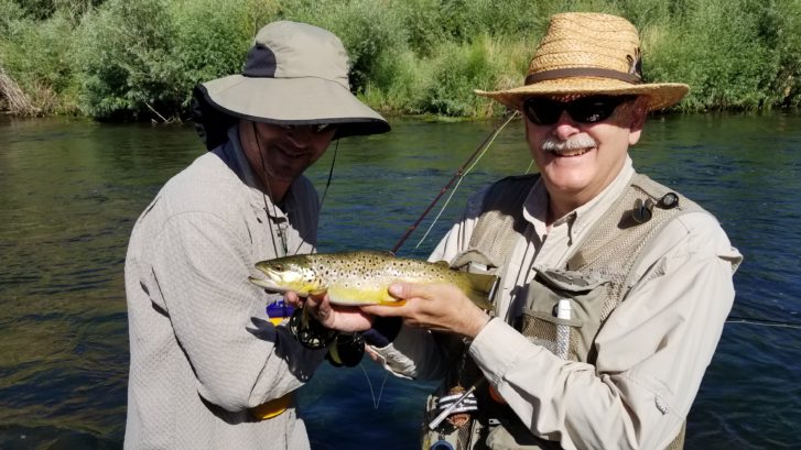 To fly Anglers hold up a wild brown trout while wading in the water