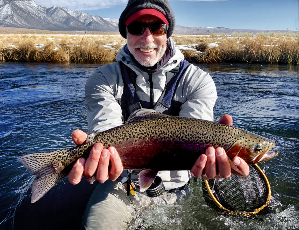 Man holds a large brightly striped Rainbow Trout over the water