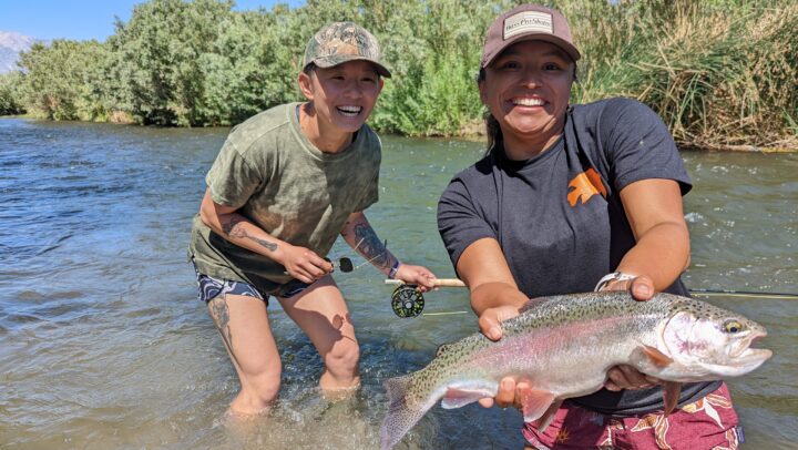 two girls hold up a large rainbow trout on the lower owens river in summertime